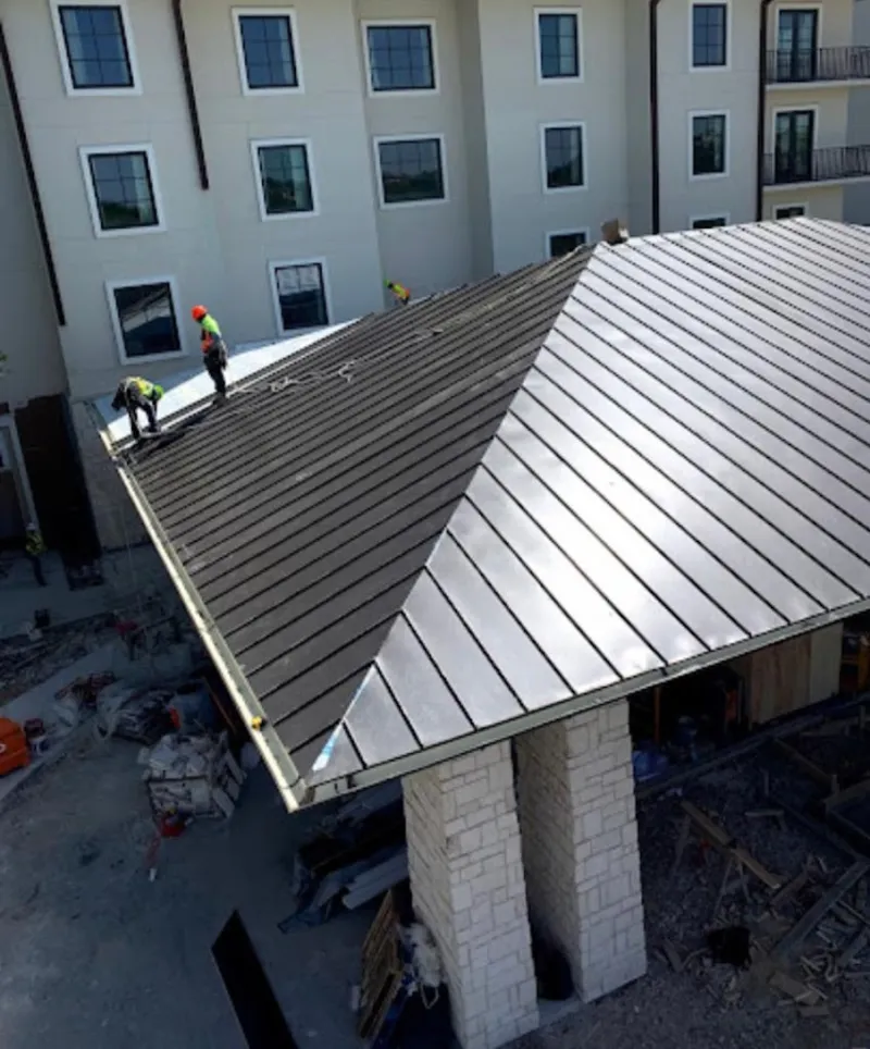 Crew installing standing seam metal roof panels on a commercial project in Mays Chapel